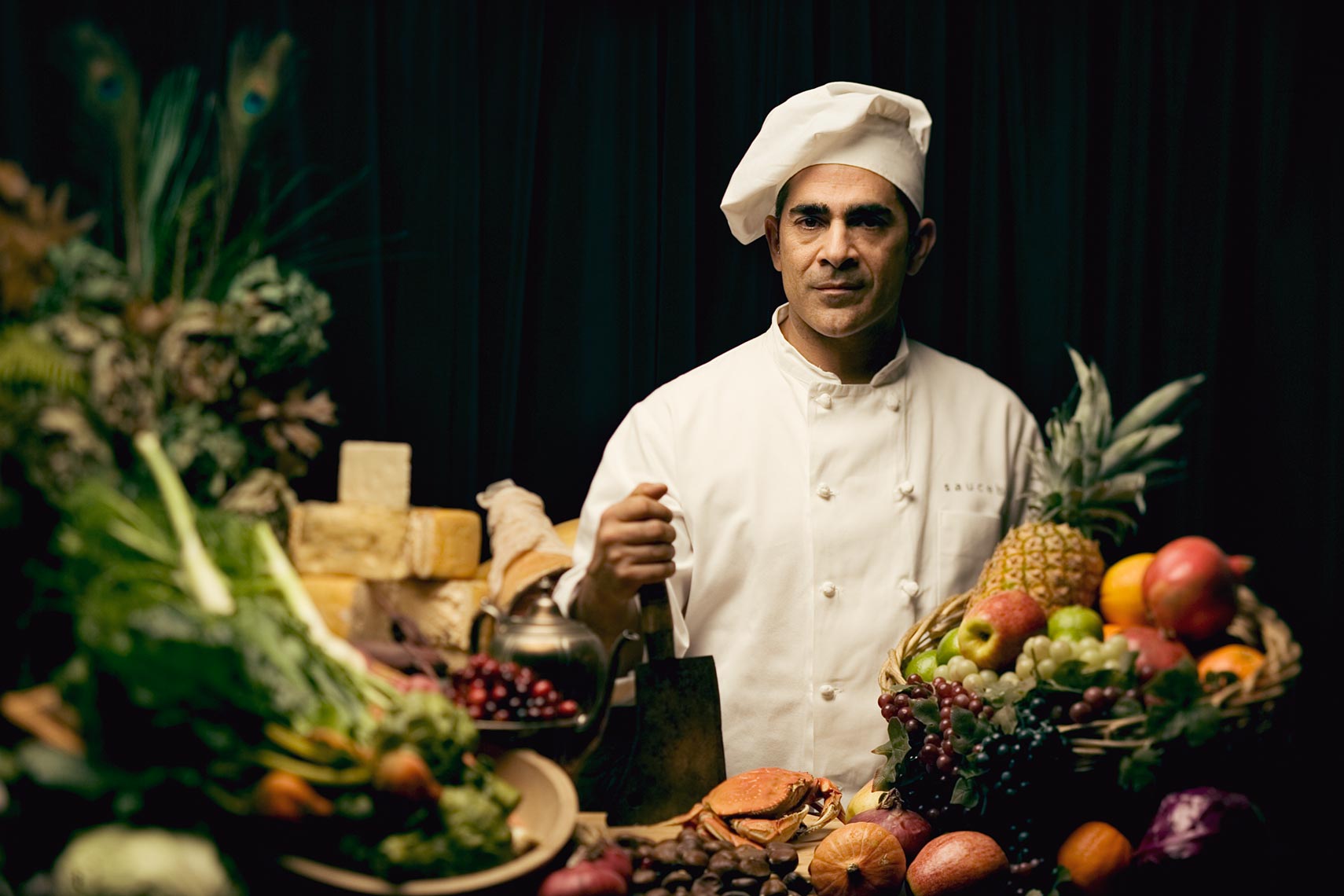 Portrait of chief surrounded by fruit and vegetables with a black background.