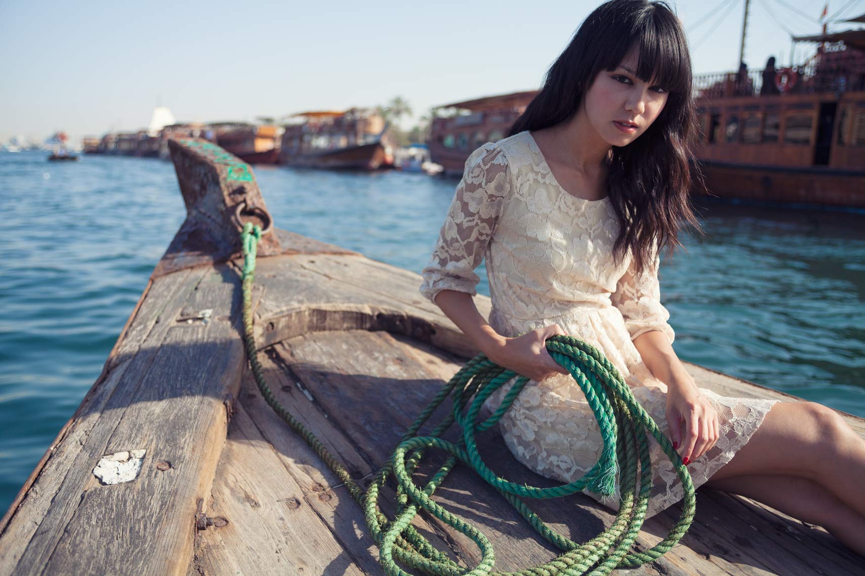 Woman sitting on a boat holding a green rope in Dubai for commercial fashion photograph.