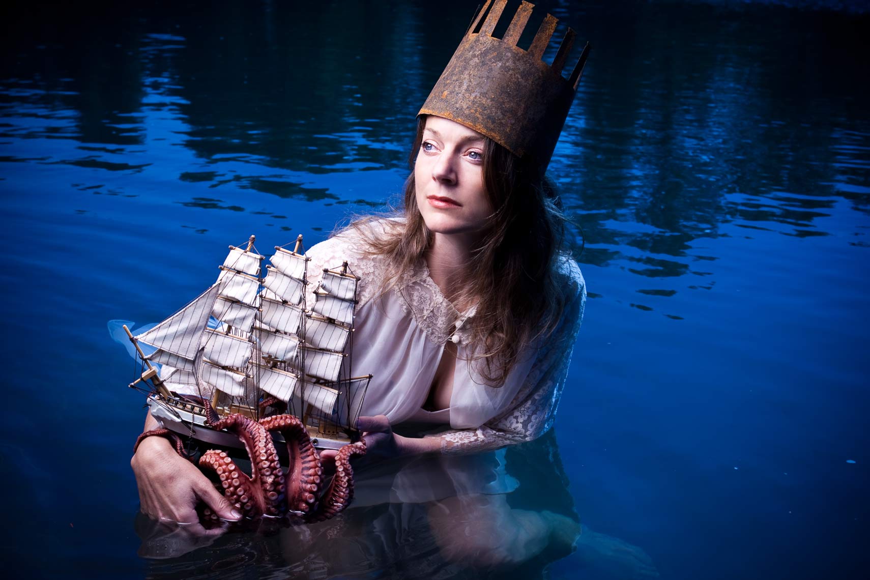 Woman in the water wearing a crown, holding a miniature boat, and an octopus.