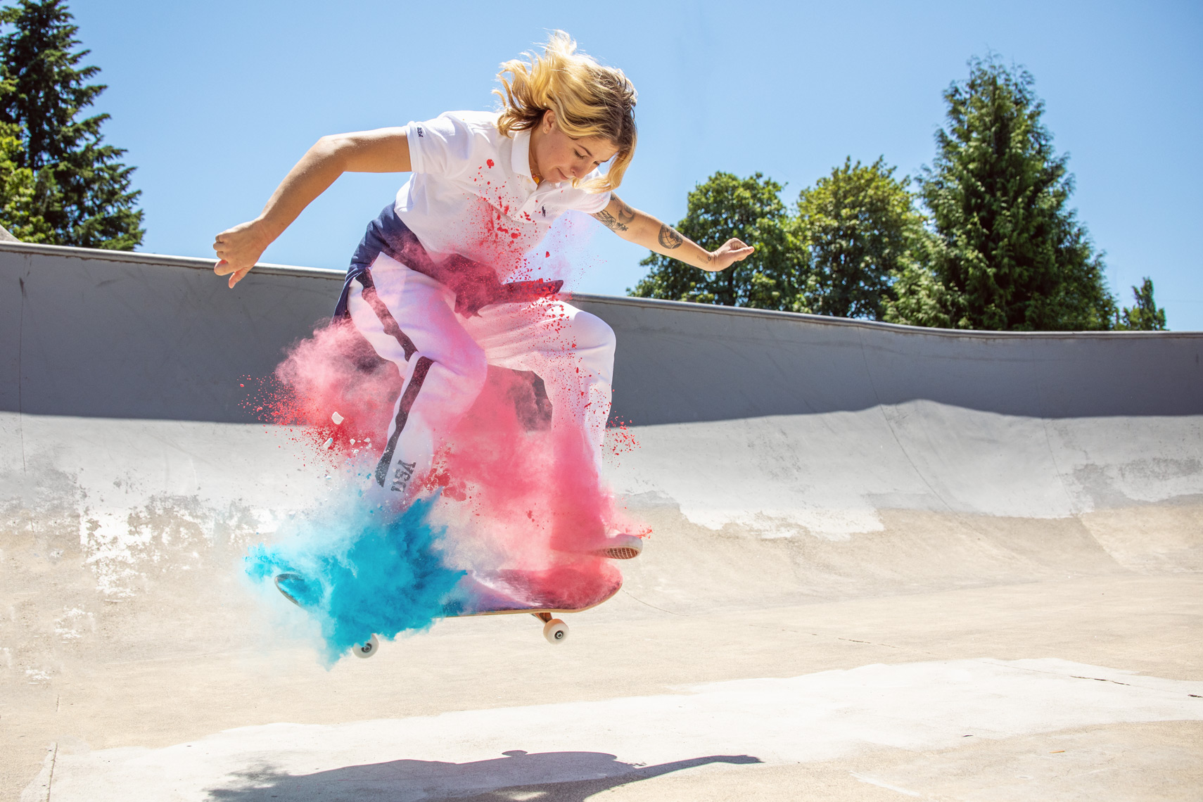 Commercial Portrait photography by Michael Schmitt - Olympic skateboarder Jordyn Barrett in the air at skate park with colored chalk exploding around her legs. 