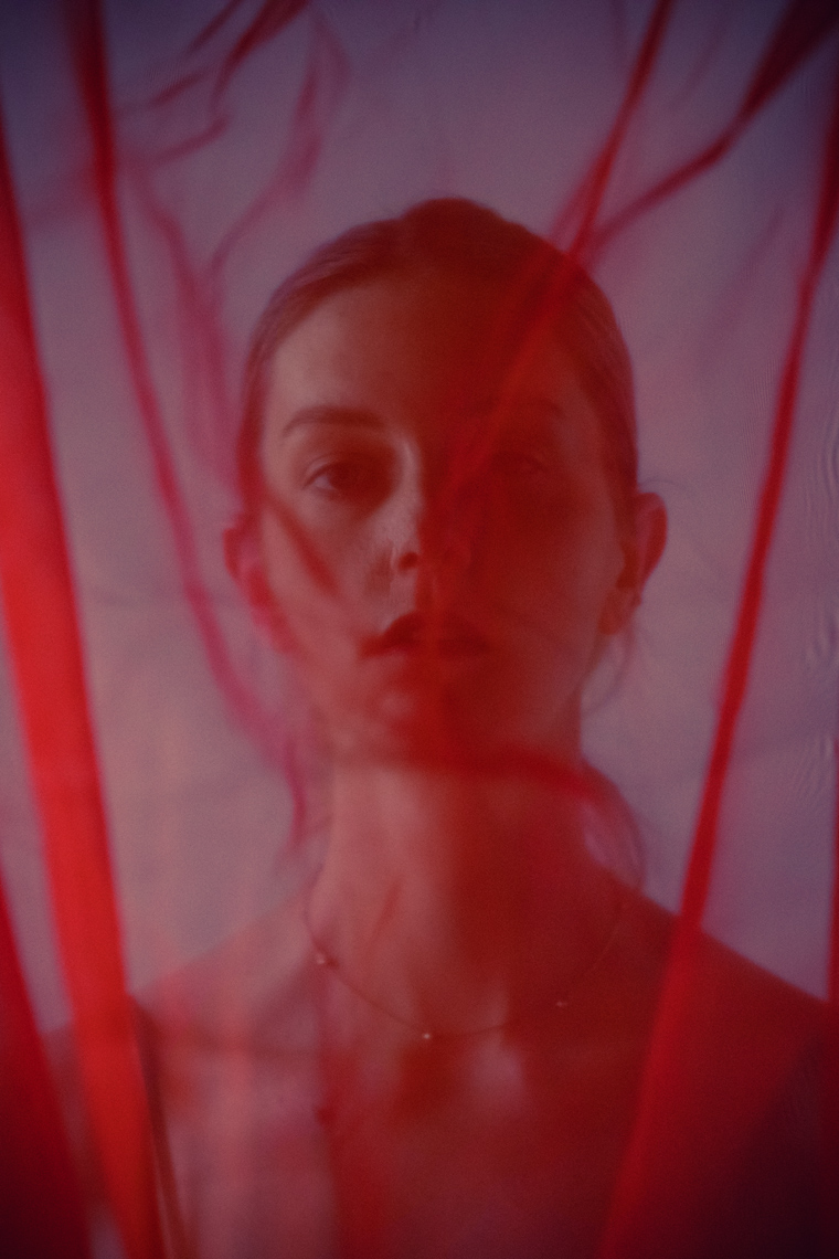 Sheer red curtain obscuring portrait of woman in studio.