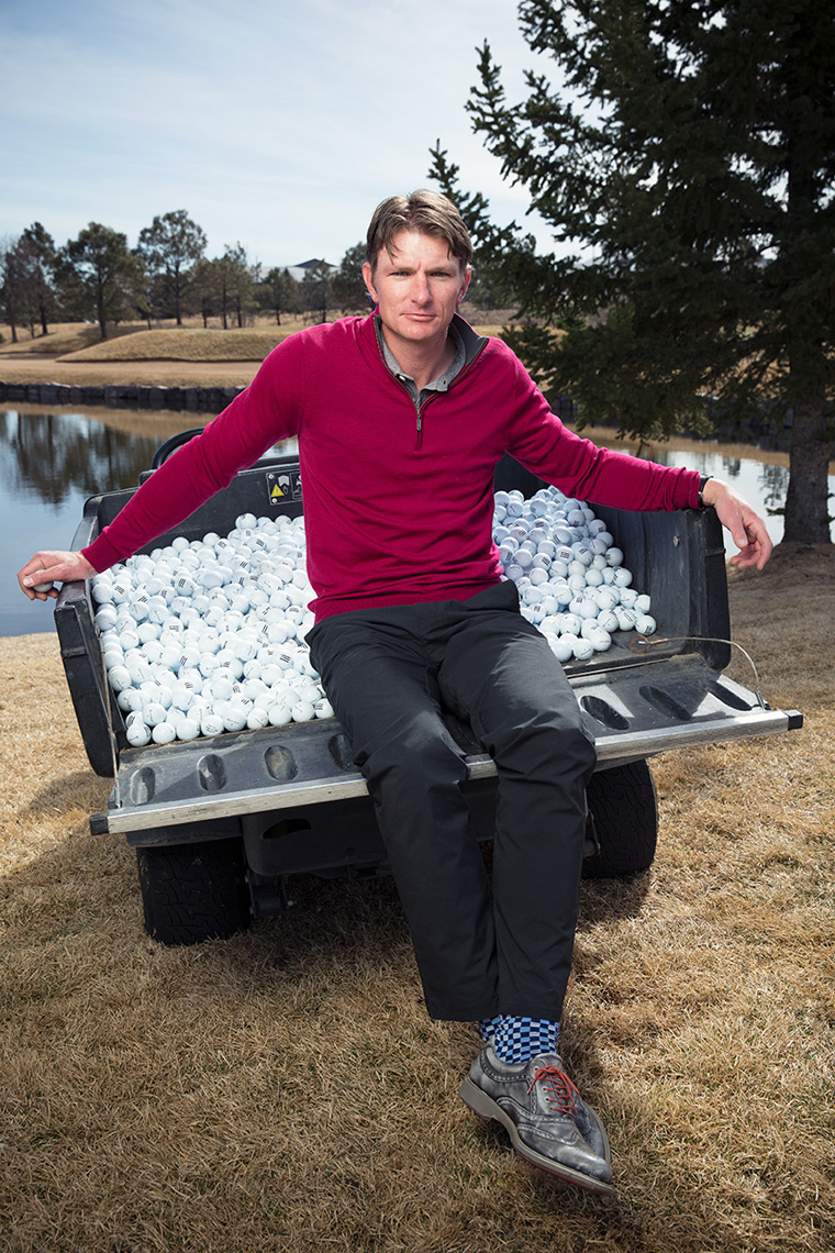 Editorial portrait of a man sitting in the back of a small truck filled with golf balls.