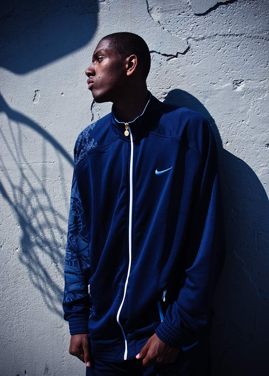 Commercial portrait of basketball player against a wall with shadow of hoop behind him.