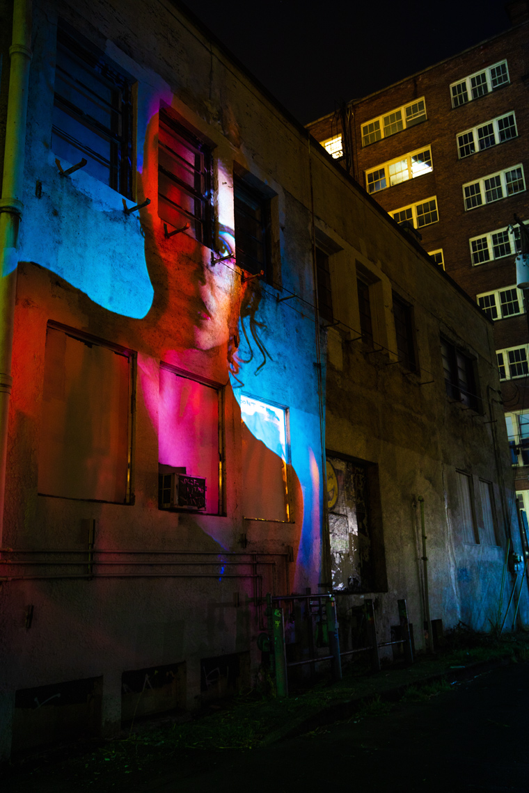 Projection of a woman with vivid colors onto a building at night in downtown Portland