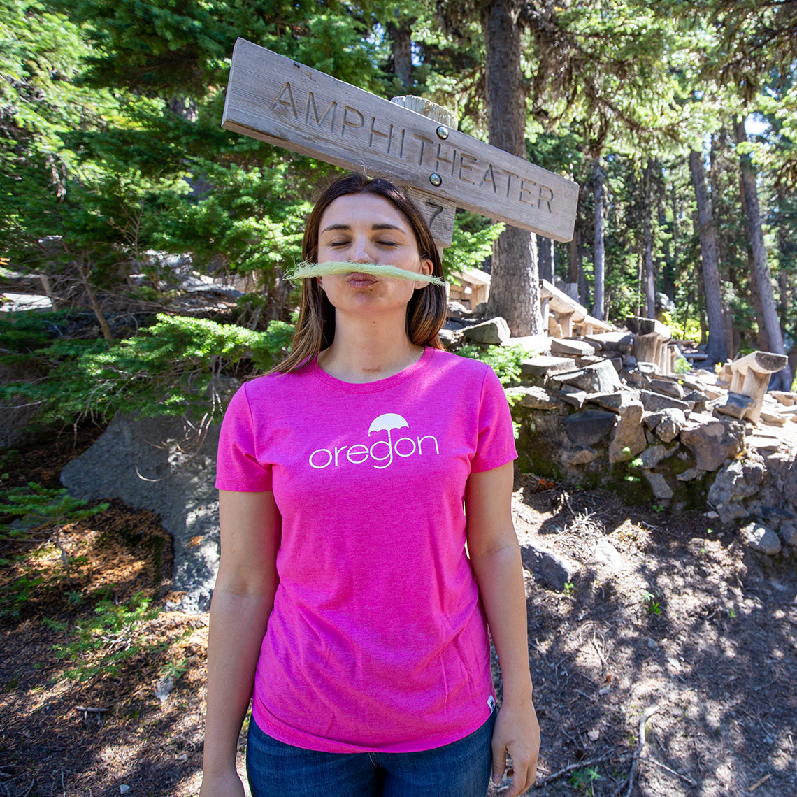 Woman with pink shirt in the mountains holding moss between her nose and lips