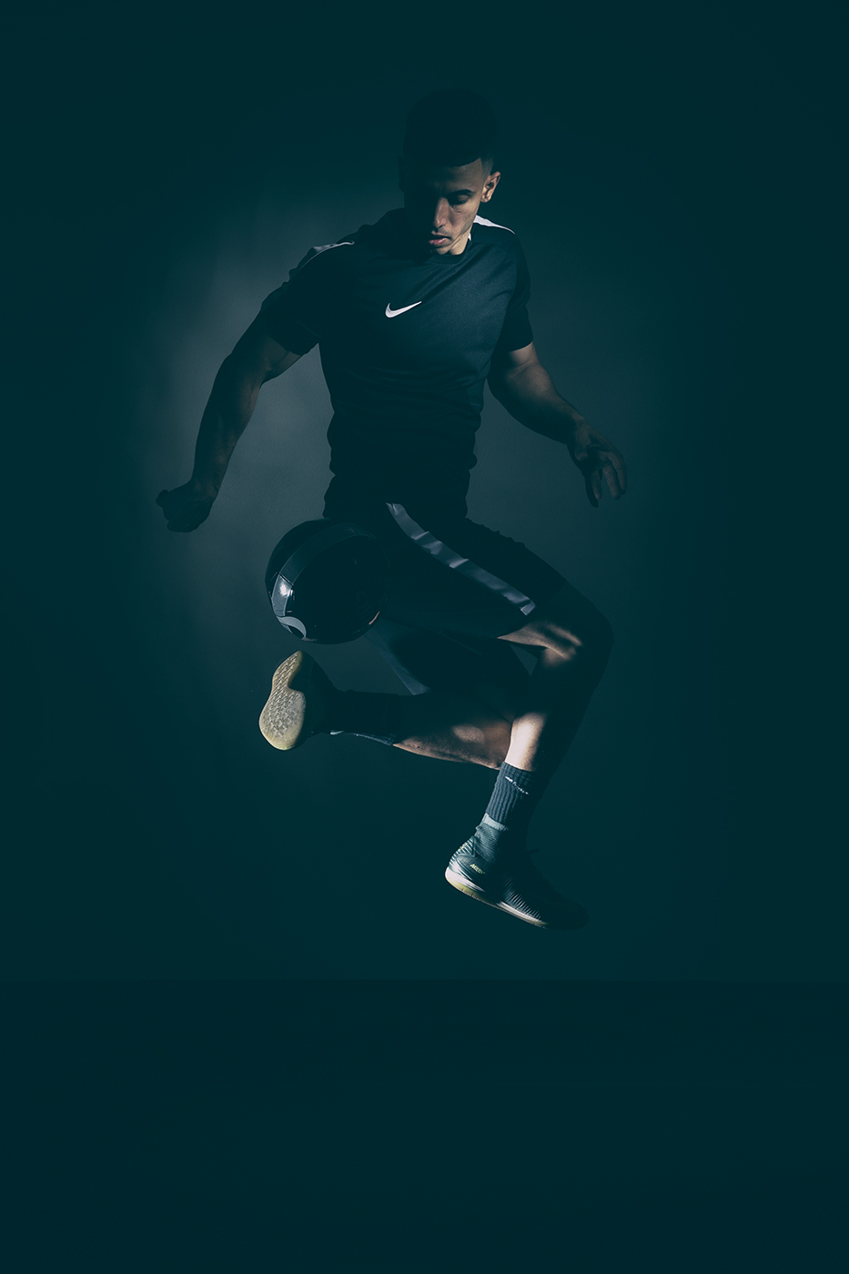 Soccer player doing a ball trick indoors with dramatic lighting on a black background.