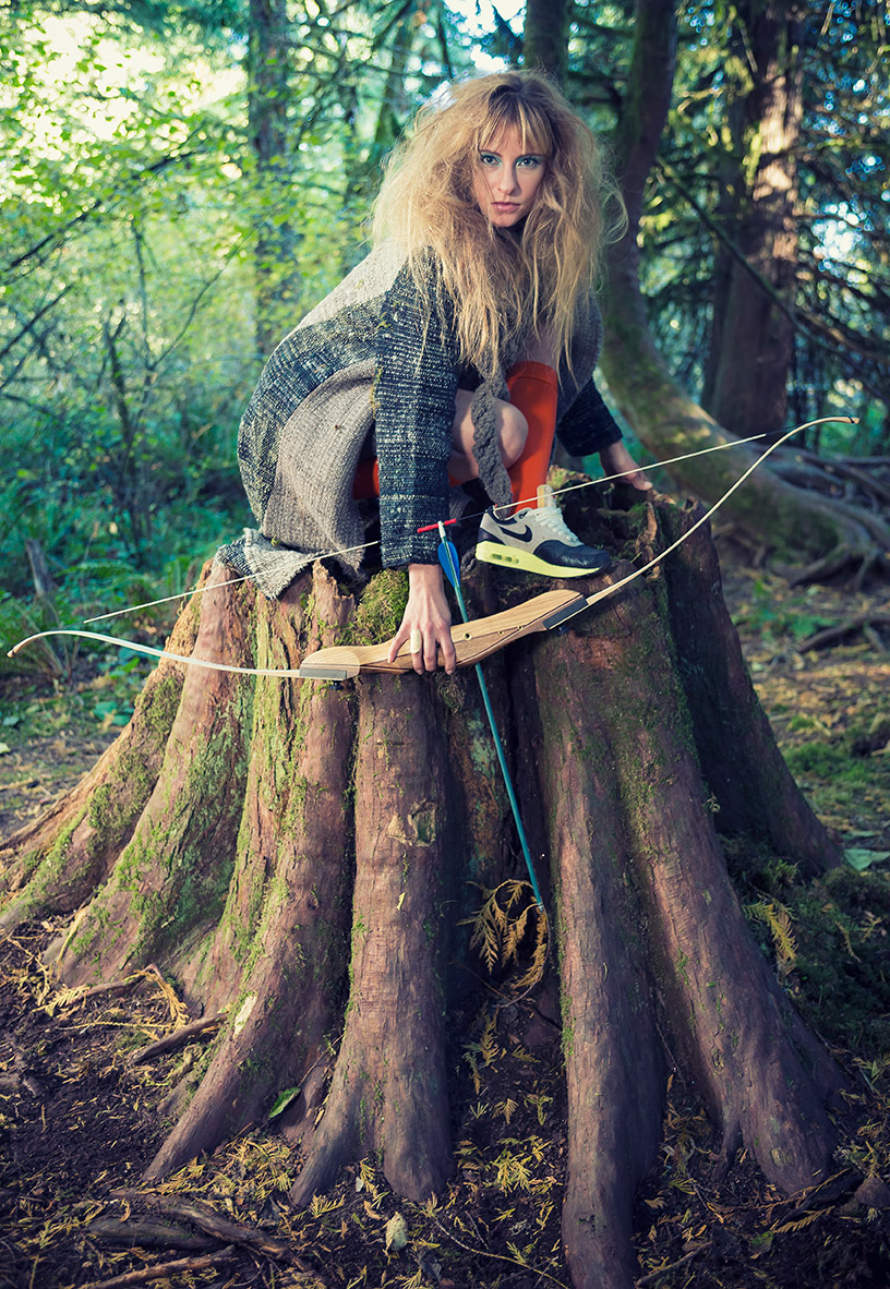Woman with bow and arrow on a large tree stomp in the Oregon forest.